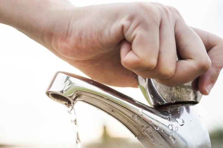 Image of a hand turning off a dripping tap with sunshine in the background