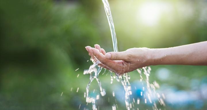 An image of an outstretched hand with water pouring into it, in an outdoor setting. 