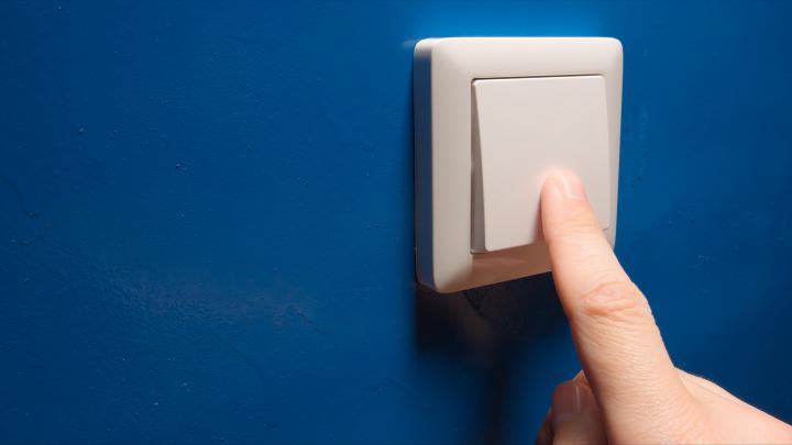 An image showing a hand flicking a large electricity switch on a blue wall