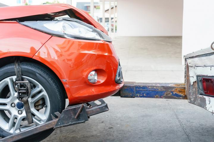 An image showing a small red car being towed behind the back of a tow truck. 