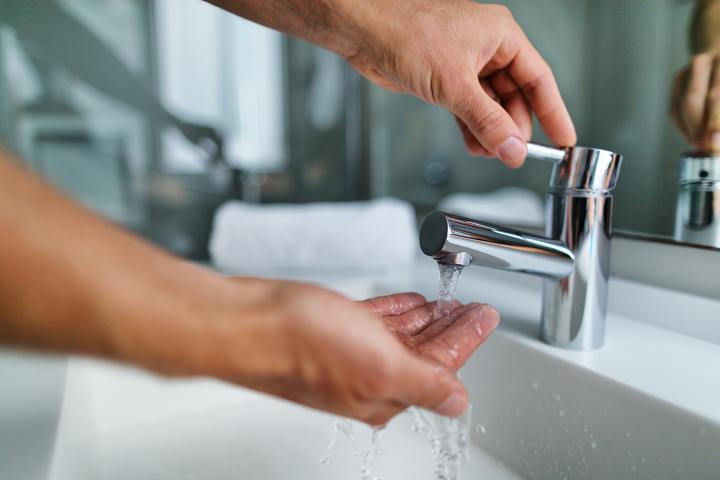 A photo showing a person's hand turning on a bathroom tap, and the person's other handing catching watching coming out of the tap.