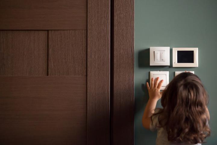 A photo showing a young girl pressing a light switch on a wall.
