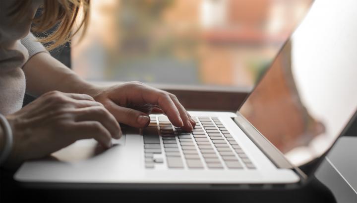 Image of a laptop. A woman's hands are visible typing on the laptop keyboard.