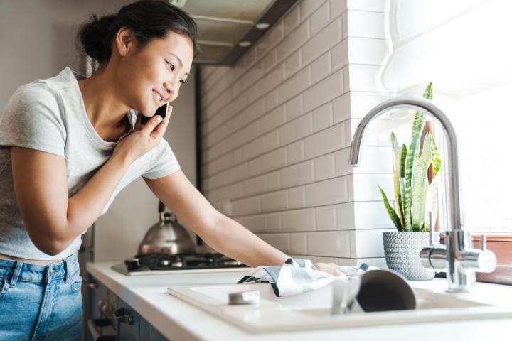 Photo of a young woman standing at her kitchen sink while on the phone.