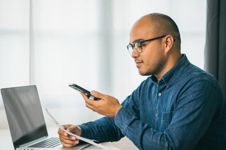 Image of a man looking at a bill while using his phone