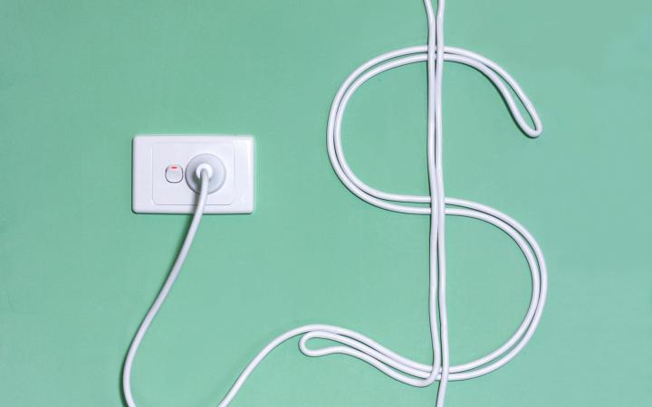 An image showing a wall socket with a power cord plugged in, in the shape of a in the dollar sign