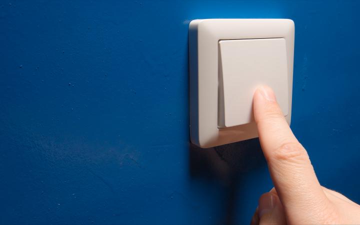 An image showing a hand flicking a large electricity switch on a blue wall