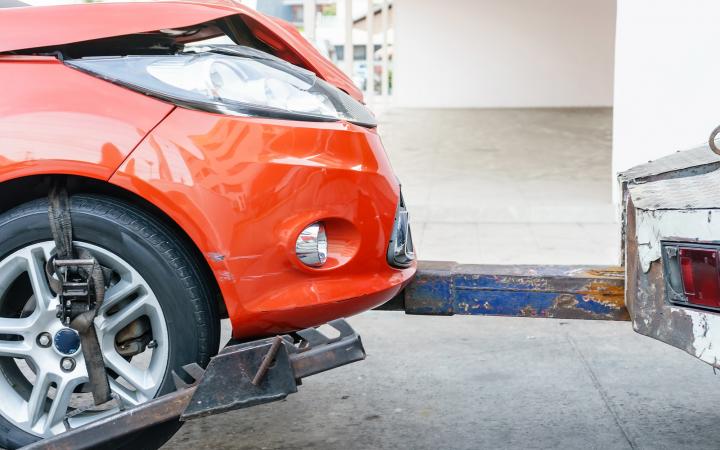 An image showing a small red car being towed behind the back of a tow truck. 