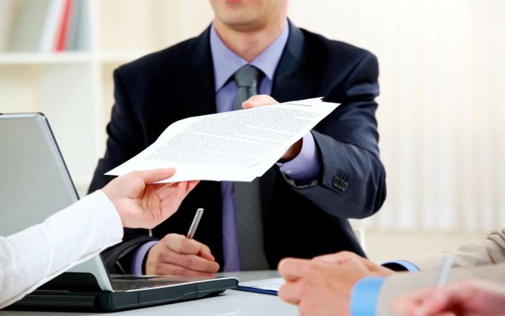 Man handing over a document to two people sitting across the desk
