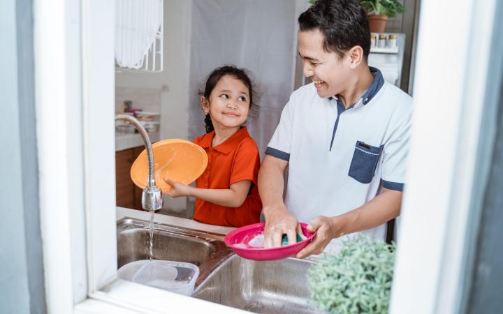 Father and his young daughter together at kitchen sink, washing dishes.