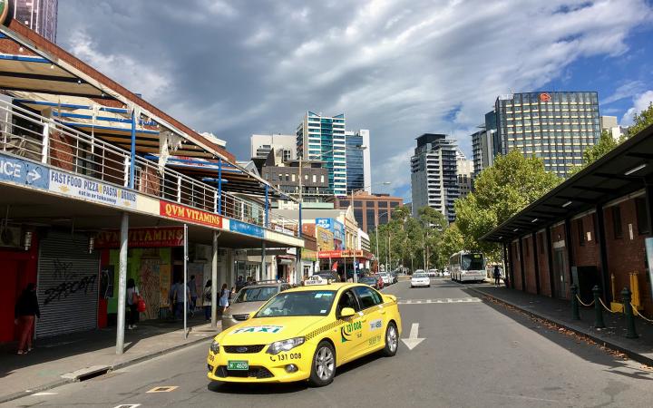 A yellow taxi drives through a back street near Melbourne’s Victoria Market.
