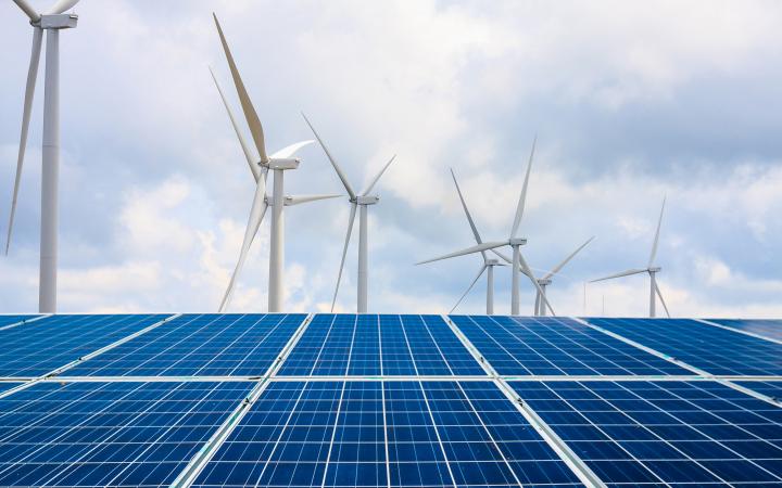 Image of solar panels in the foreground, with wind turbines in the background.