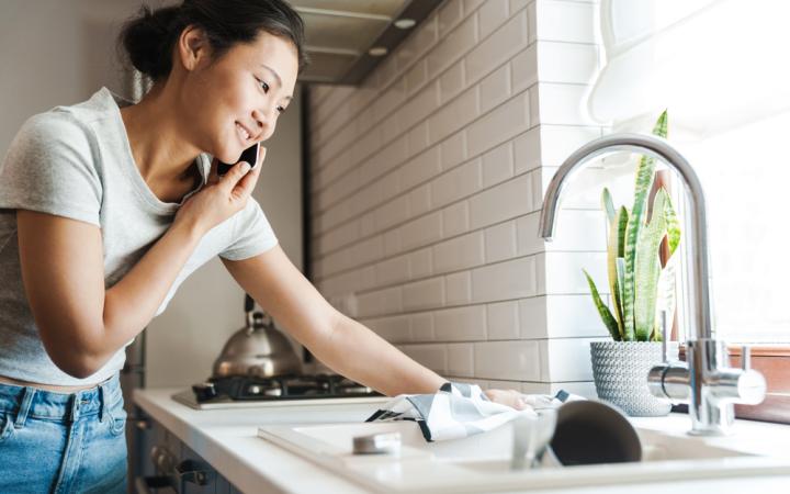 Photo of a young woman standing at her kitchen sink while on the phone.