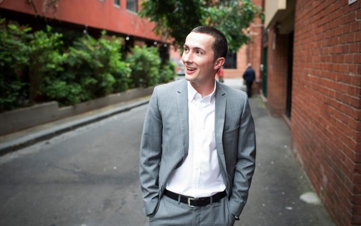An image of Jonathan, transport team member at the commission, standing in a Melbourne laneway and smiling at something off-camera. 