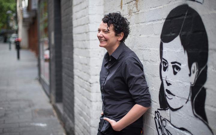 Kate, an Essential Services Commission employee, leaning against a wall decorated, graffiti-style, with the image of a woman. Kate is laughing at some off-camera.