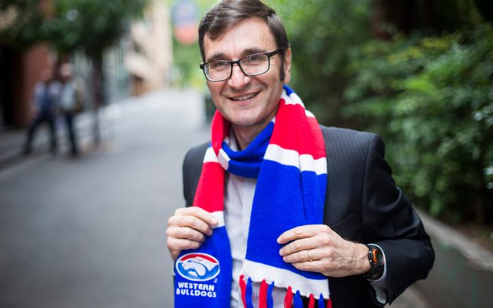 An photo of Jeff, a VEET team member at the commission, wearing a Western Bulldogs scarf and standing in a Melbourne laneway smiling at the camera.