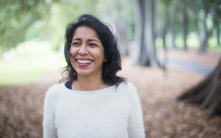 An image of Angeline, water team member at the Essential Services Commission, standing in a garden and smiling at something off-camera.