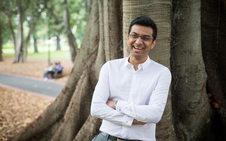 An image of Jaawid, water team member at the commission, leaning against a tree in a Melbourne park and smiling. 