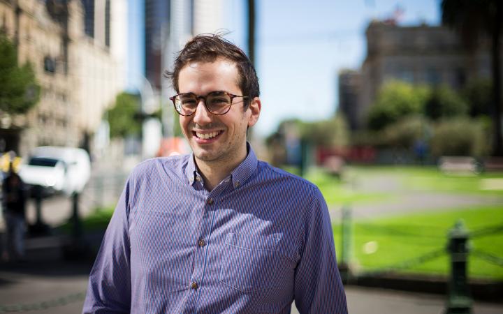 Matthew, an Essential Services Commission employee, in a city street with a garden in the background. He is smiling at the camera.