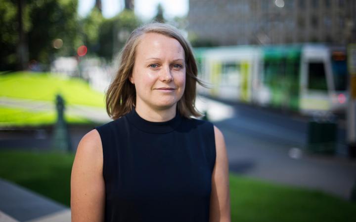 Image showing Sandra, VEET team member at the Essential Services Commission, on a city street with a garden and a tram in the background.