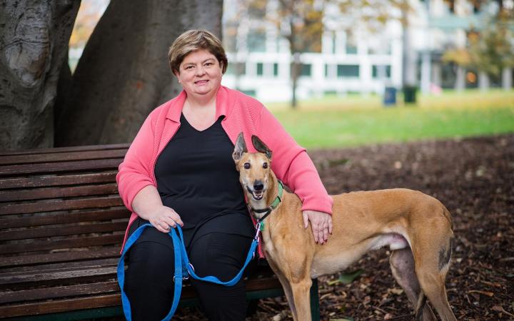 An image of Merryn, local government team member, sitting on a park bench with her tan-coloured greyhound, Jake, standing next to her.
