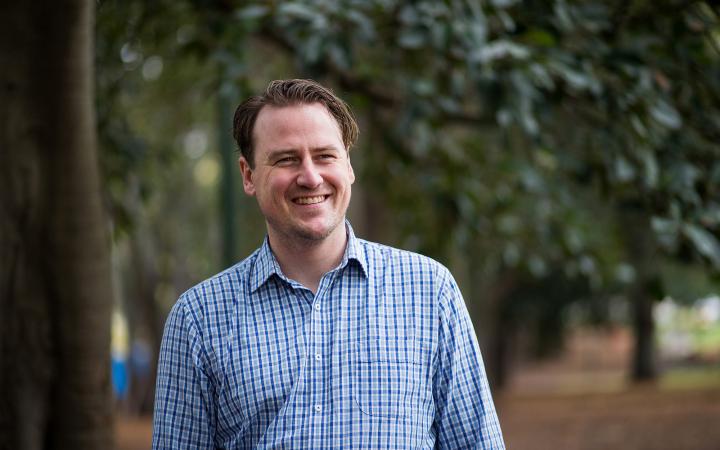 An image of Sam, strategic communication team member at the Essential Services Commission, standing in a park and smiling at something off-camera.