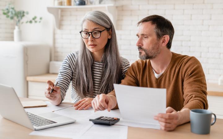 A middle aged couple looking at bills together, at a kitchen table