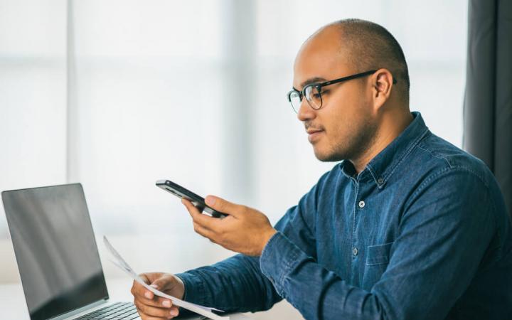 Image of a man looking at a bill while using his phone