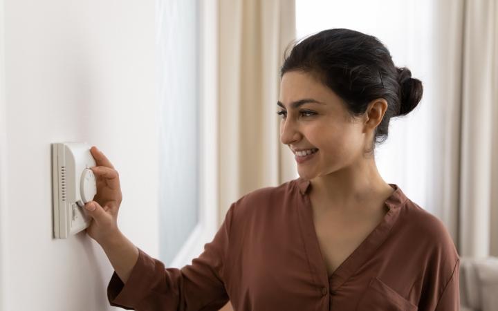 A woman adjusting her thermostat on the wall and smiling